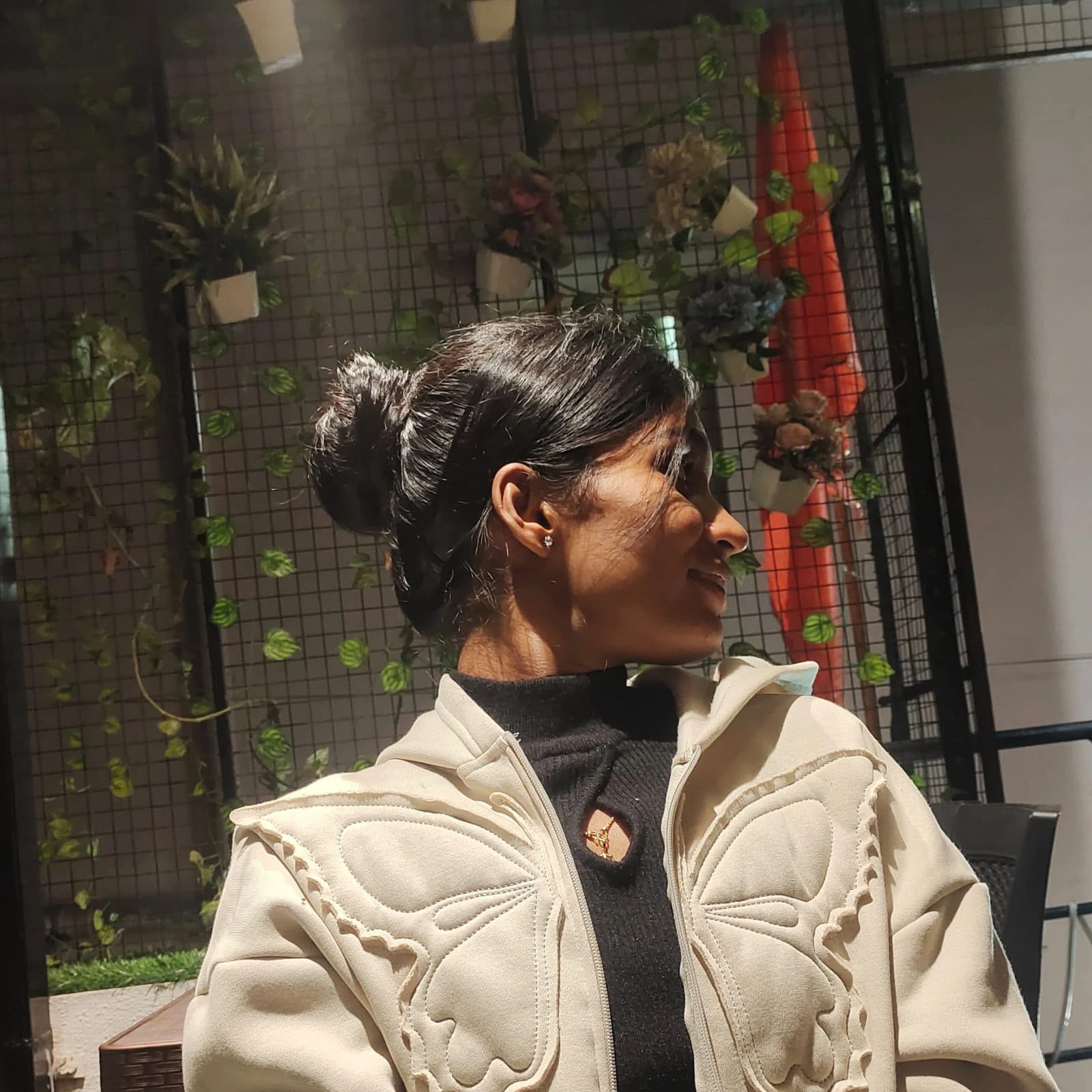 You looking to the side in warm sunlight, wearing a cream butterfly jacket.