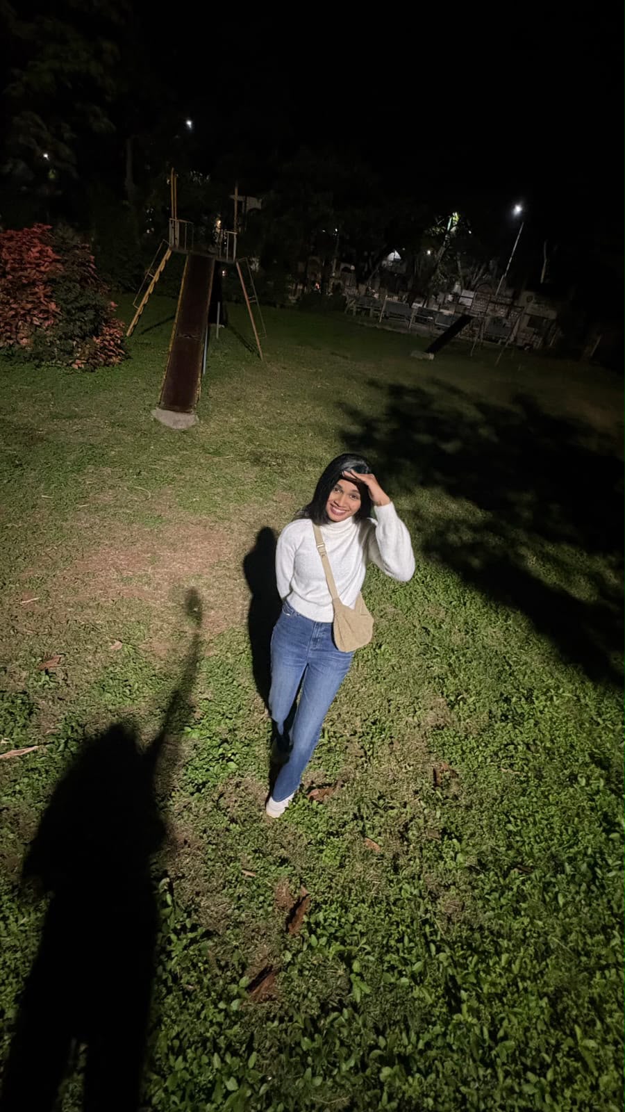 You smiling in a night-time park in a white sweater and jeans.