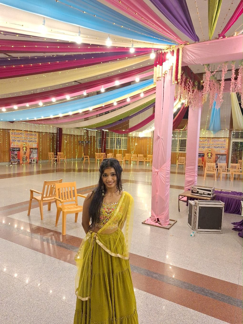 You standing beneath colorful draped lights in your green traditional outfit.