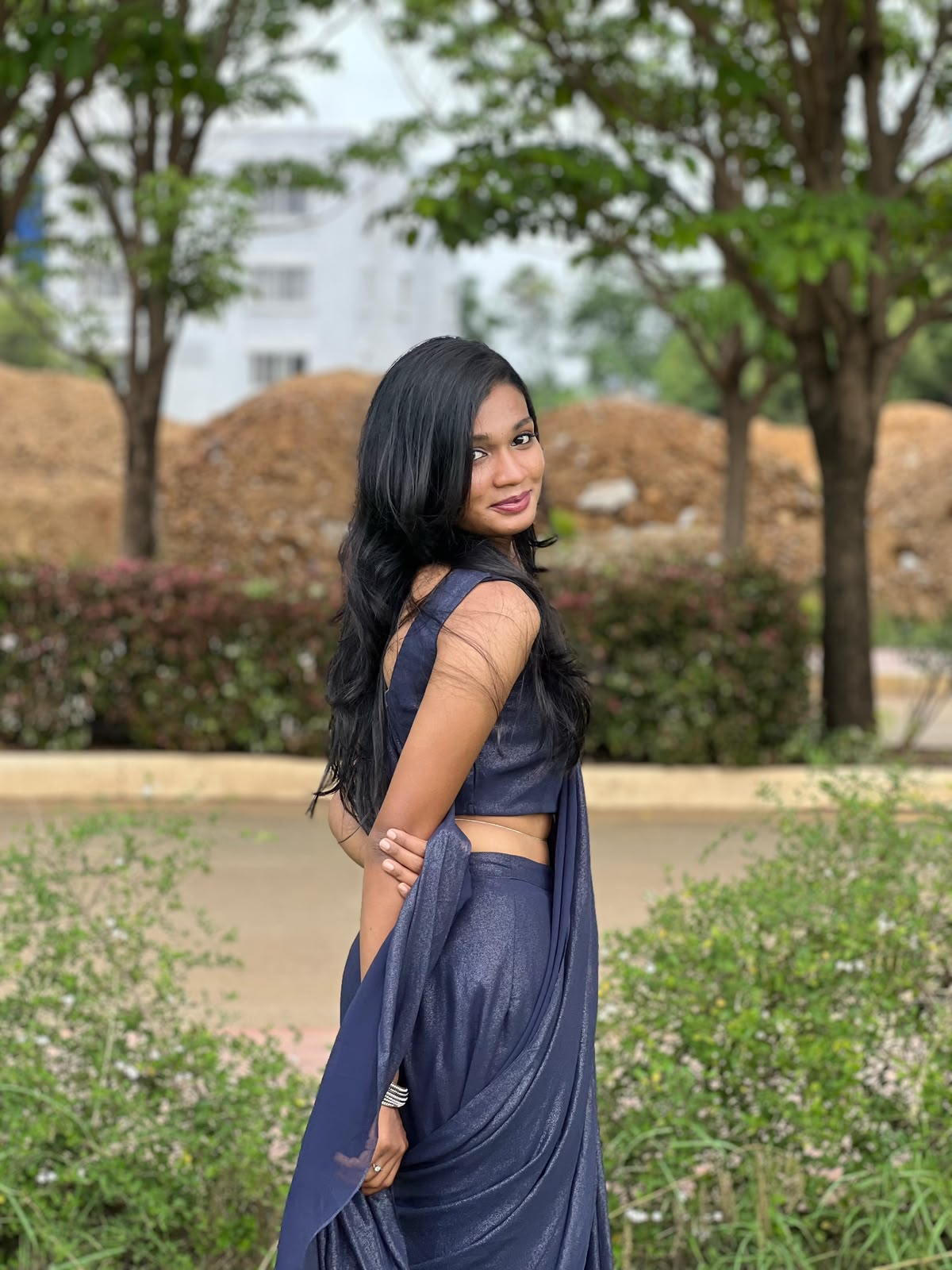 You looking back with a smile in an elegant navy sari outdoors.
